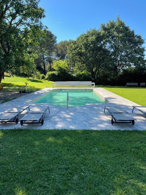 Ein rechteckiger Pool mit glasklar blauem Wasser, umgeben von einer Betonplattform. Auf gegenüberliegenden Seiten des Pools stehen zwei Liegestühle.