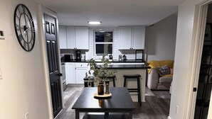 A modern kitchen with white cabinets, a dining table with two chairs, and a large clock on the wall.