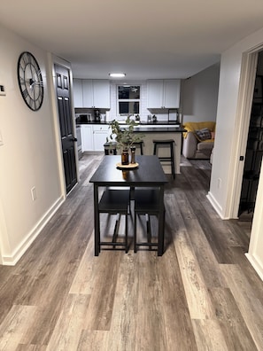 A modern kitchen with white cabinets, a dining table with two chairs, and a large clock on the wall. - Buckeye Lake Retreat w/ Fire pit/ Sleeps 8 (Thornville)