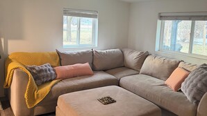 A modern living room with a sectional sofa, ottoman, and a hanging light fixture.