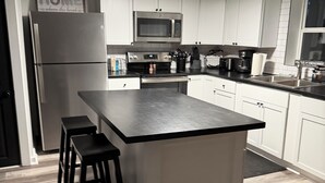 A modern kitchen with white cabinets, a stainless steel refrigerator, a microwave, and a central island with stools.
