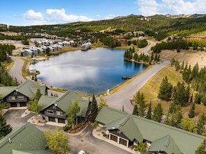 A residential area with a large lake, multiple houses, and a road. - Big Sky Escape | Ski In/Ski Out + Mountain Views (Big Sky)