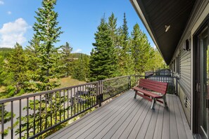 A wooden deck with a bench, surrounded by a metal railing, overlooking a forested area. - Big Sky Escape | Ski In/Ski Out + Mountain Views (Big Sky)