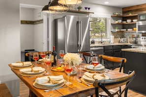 A modern kitchen with stainless steel appliances, a wooden dining table set for six, and a view of the outdoors through a window. - Big Sky Escape | Ski In/Ski Out + Mountain Views (Big Sky)