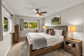 A bedroom with a wooden bed, two bedside lamps, a ceiling fan, and a window with a view of greenery. - Big Sky Escape | Ski In/Ski Out + Mountain Views (Big Sky)