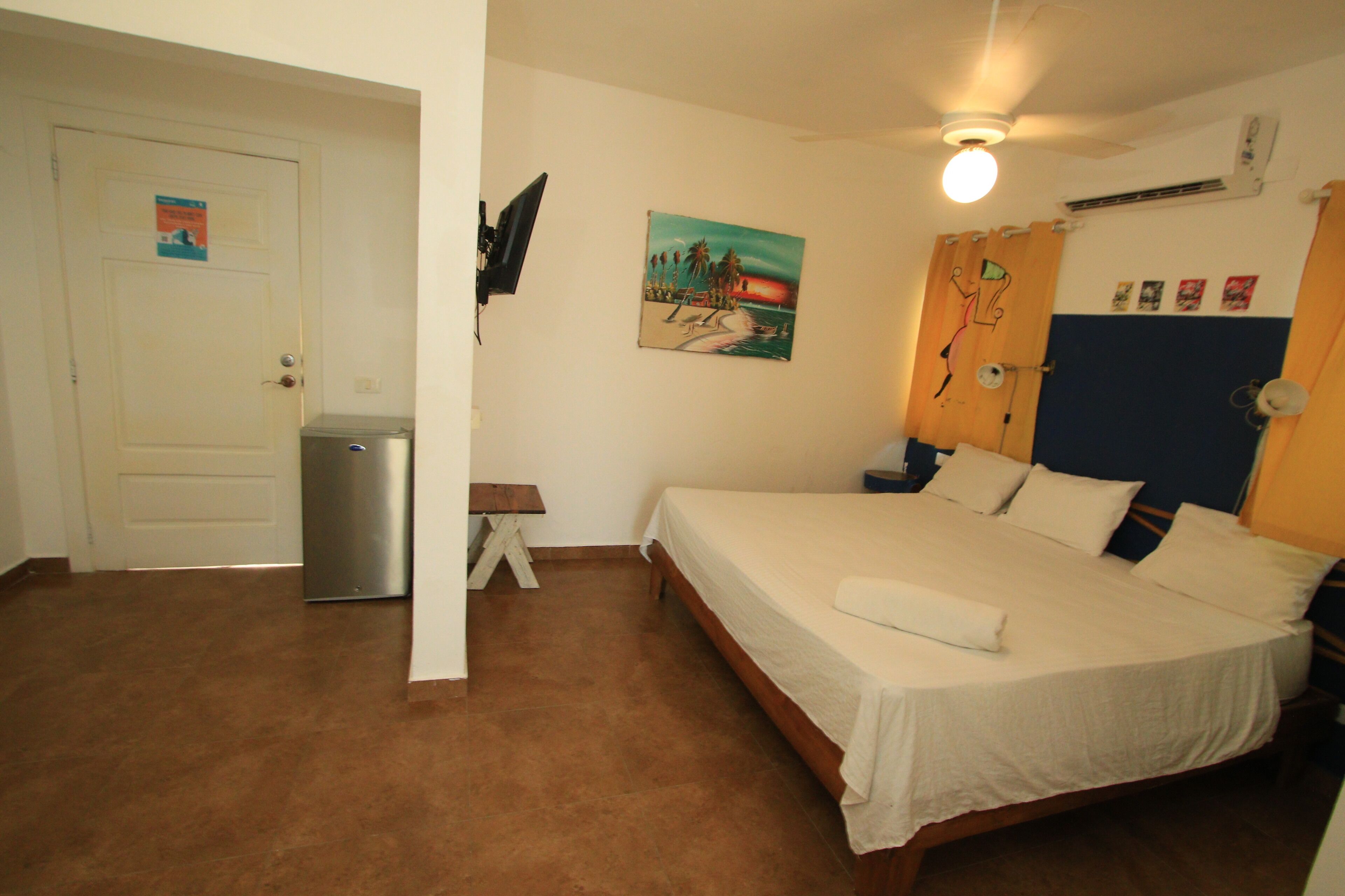Ein Schlafzimmer mit einem Bett, einem kleinen Tisch, einem an der Wand befestigten Fernseher und einer Tür.