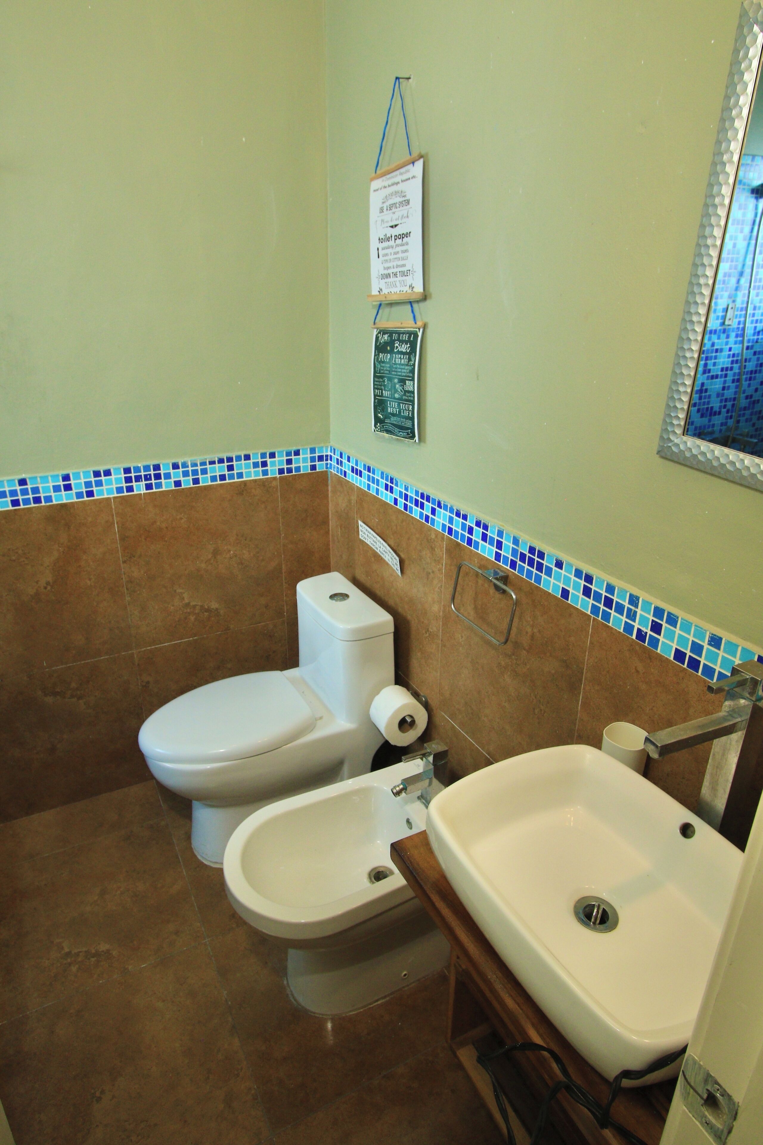 Un bany amb vàter, bidet, rentapel orelles i parets de rajola.