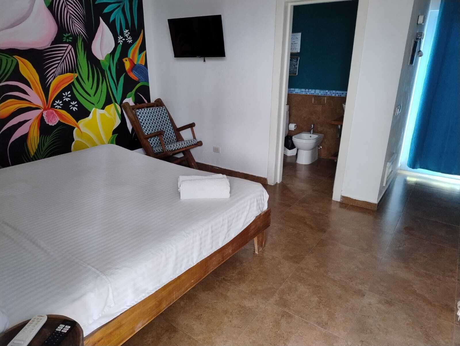 Ein Hotelzimmer mit Bett, Sessel, Fernseher und einem durch eine offene Tür einsehbaren Badezimmer.