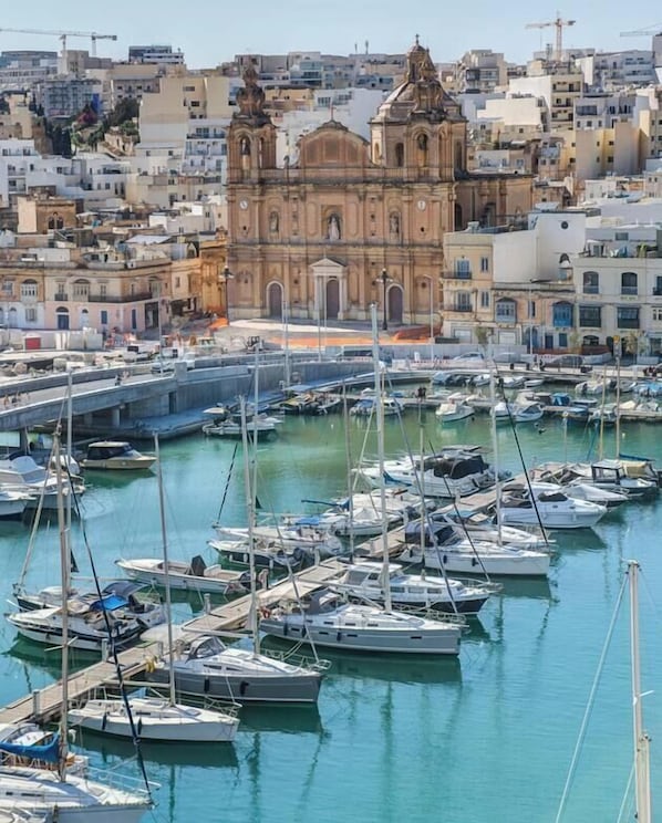 Ein Yachthafen mit vor Anker liegenden Booten, eine markante Kirche im Hintergrund und eine Stadtansicht.