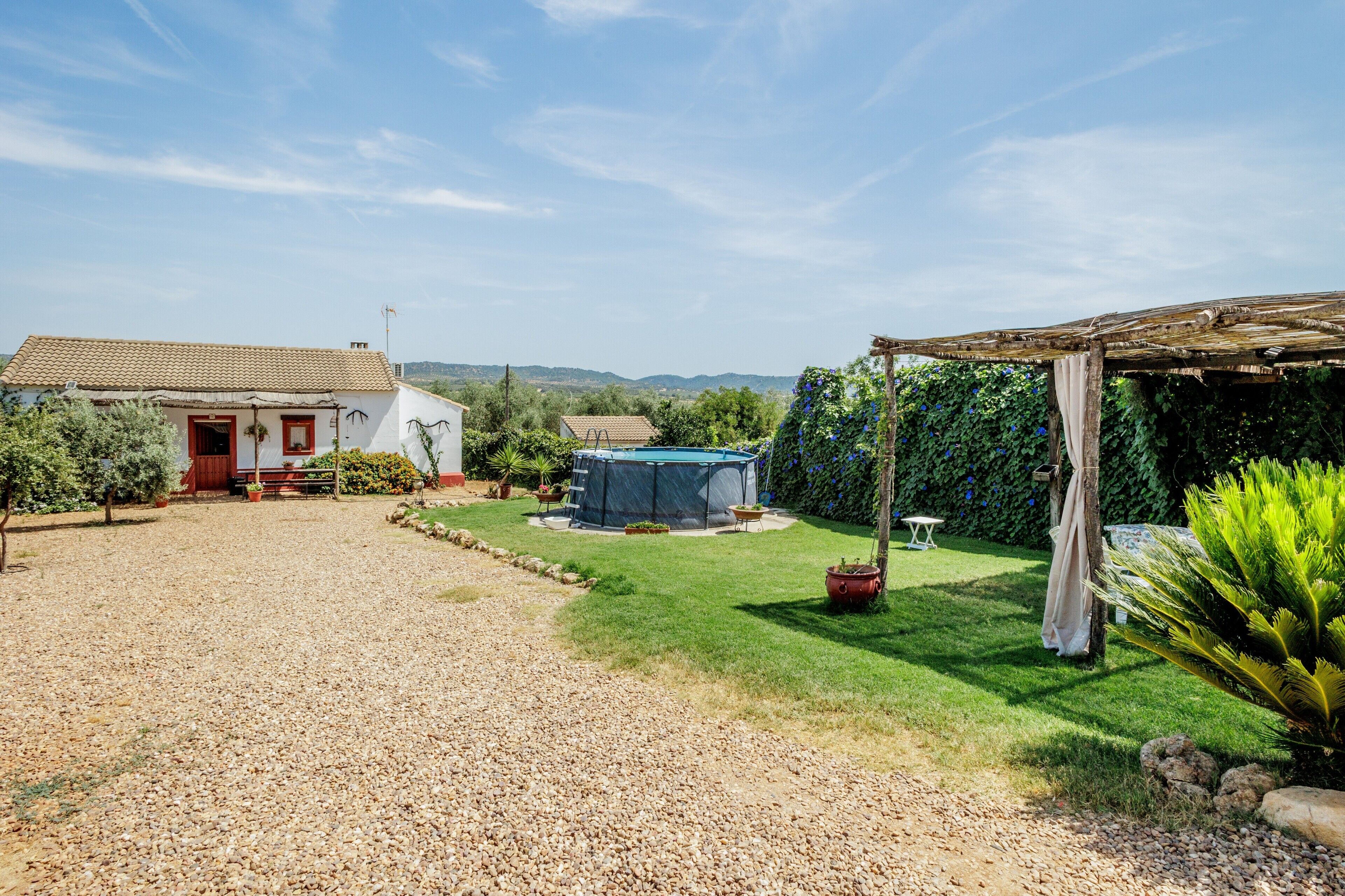A house with a gravel driveway, a covered outdoor seating area, and a fenced garden.