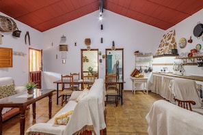 Een gezellige woonkamer met een eethoek, een keuken met hangende pannen, en een hoog plafond met houten balken.