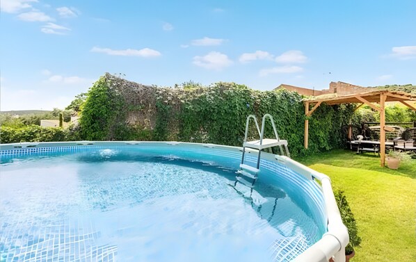 Ein Schwimmbecken mit Holzterrasse und einer Pergola, umgeben von üppiger Bepflanzung.
