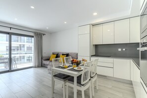 Eine moderne Küche mit weißen Schränken, einem Esstisch mit Stühlen und einem Balkon mit einer Sitzecke.