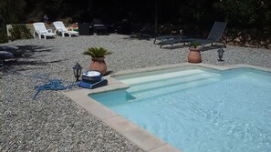 Ein Pool mit Kiesrand, Liegestühlen und einer kleinen Gartenanlage mit Topfpflanzen.