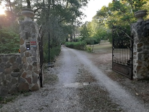 Ein Kiesweg führt zu einem verschlossenen Eingang mit Steinmauern und einem Metallgitter.