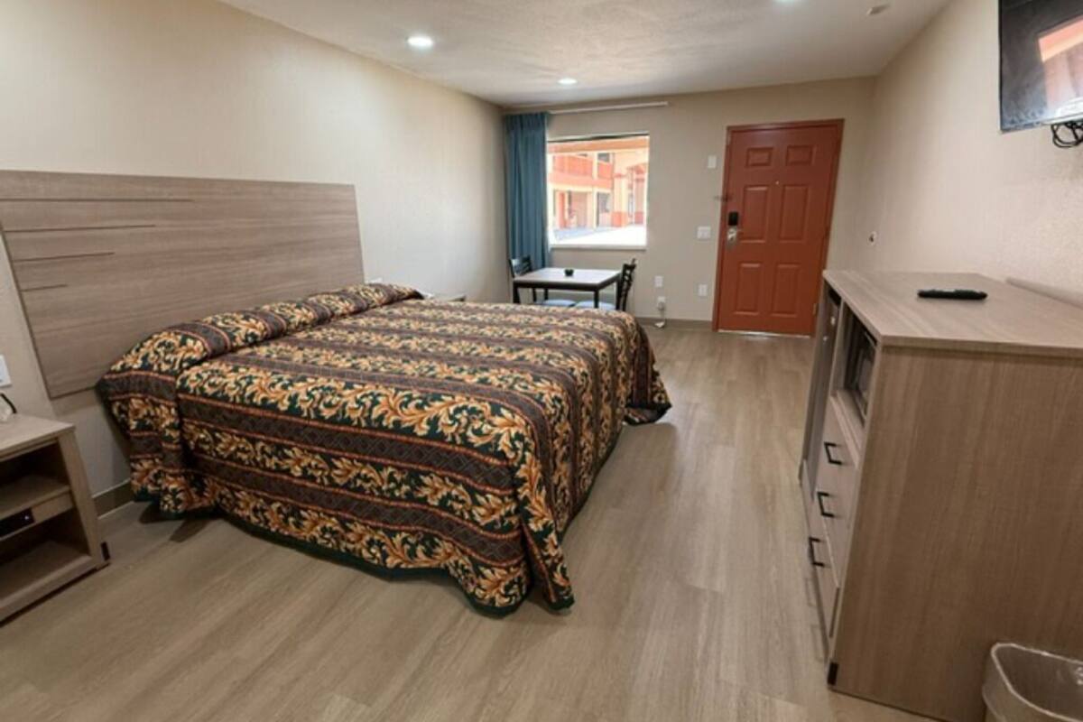A hotel room with a bed, a desk, a chair, a window, and a door.