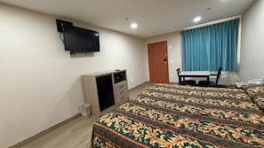 A hotel room with a bed, a TV mounted on the wall, a desk, and a window with curtains. - Town INN (Houston)