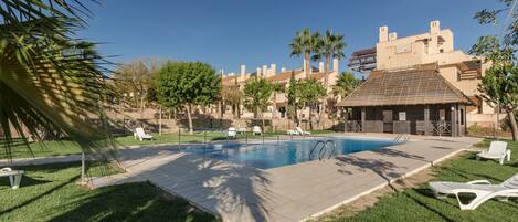 A swimming pool with lounge chairs, palm trees, and a building with a tiled roof.