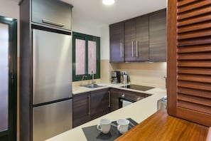A modern kitchen with stainless steel appliances, dark wooden cabinets, and a countertop with two white mugs.