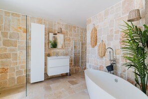 Ein Badezimmer mit Steinwand, Waschbecken in Weiß, Spiegel, Handtuchhalter und einer großen Pflanze.