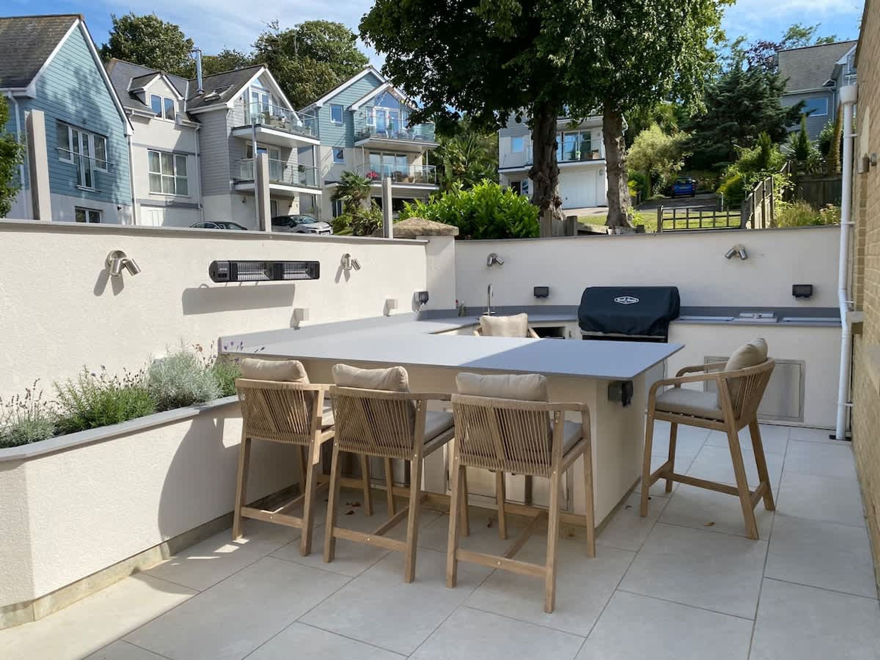 Um pátio externo com mesa, cadeiras, churrasqueira e vista para as casas vizinhas.