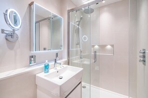 Ein modernes Badezimmer mit einer gläsernen Duschkabine, einem weißen Waschbecken mit Spiegel und einer Seifenspender.