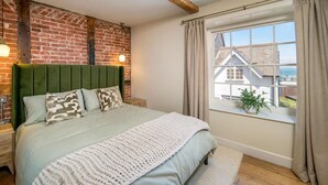 Ein Schlafzimmer mit Backsteinwand, einem grünen Kopfteil, einem großen Fenster mit Vorhängen und Blick auf ein Haus.