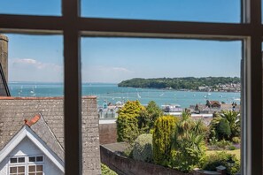 Blick durch ein Fenster auf die Küste, mit einem Yachthafen, Booten, einer fernen Insel und einer Mischung aus Wohn- und Geschäftsgebäuden.