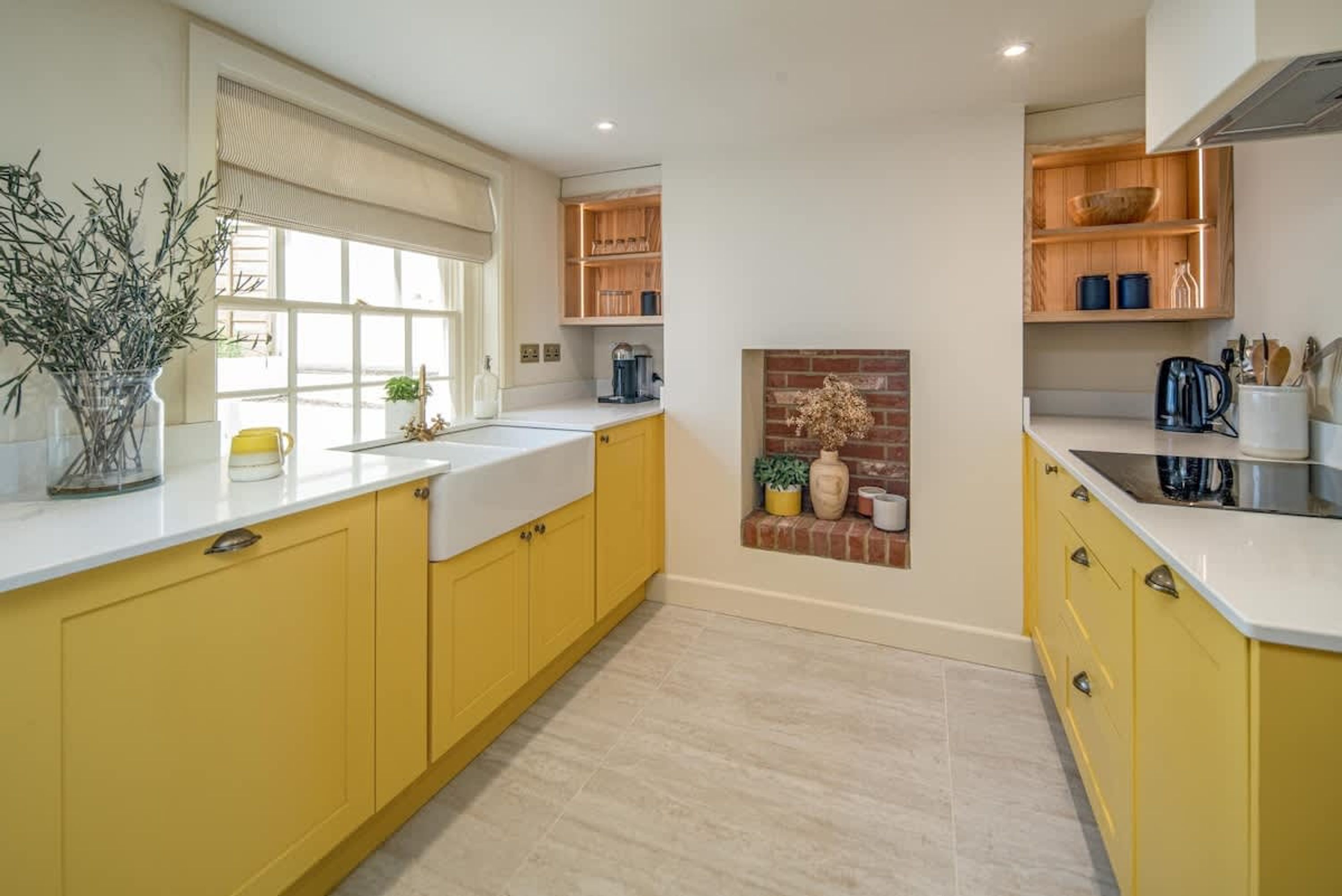 A kitchen with yellow cabinets, a white countertop, a window with blinds, and a brick fireplace.