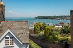 Blick auf die Küste mit einem Yachthafen, einem weißen Gebäude mit Dachfenster und üppiger Vegetation.