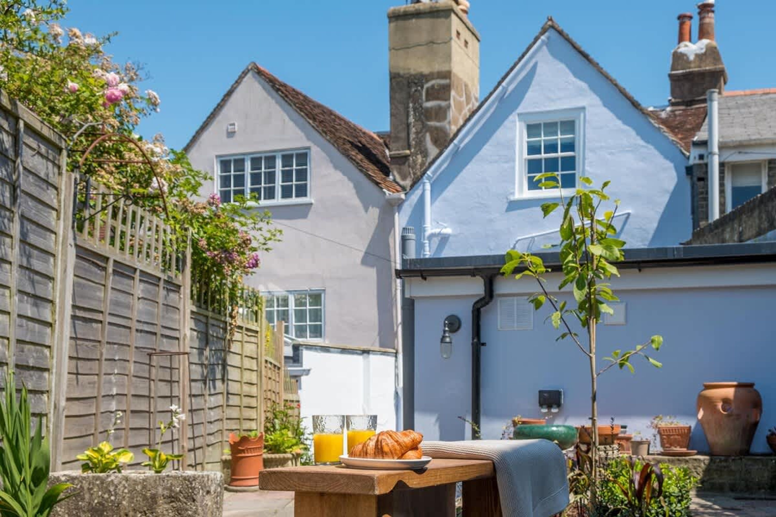 A traditional building with a white facade, a wooden fence, and a table with croissants and a glass of orange juice.