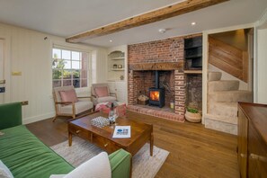Ein gemütliches Wohnzimmer mit Kamin aus Backstein, einem grünen Sofa, einem Couchtisch aus Holz und einer Treppe.