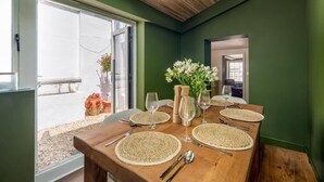 Ein Esstisch ist mit Platzsets, Weingläsern und Besteck gedeckt, mit Blick ins Freie durch eine Glastür.