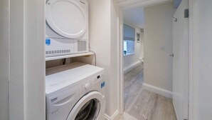 Een wasserette met een voorlader wasmachine en droger, een klein plankje en een deur naar een andere kamer.