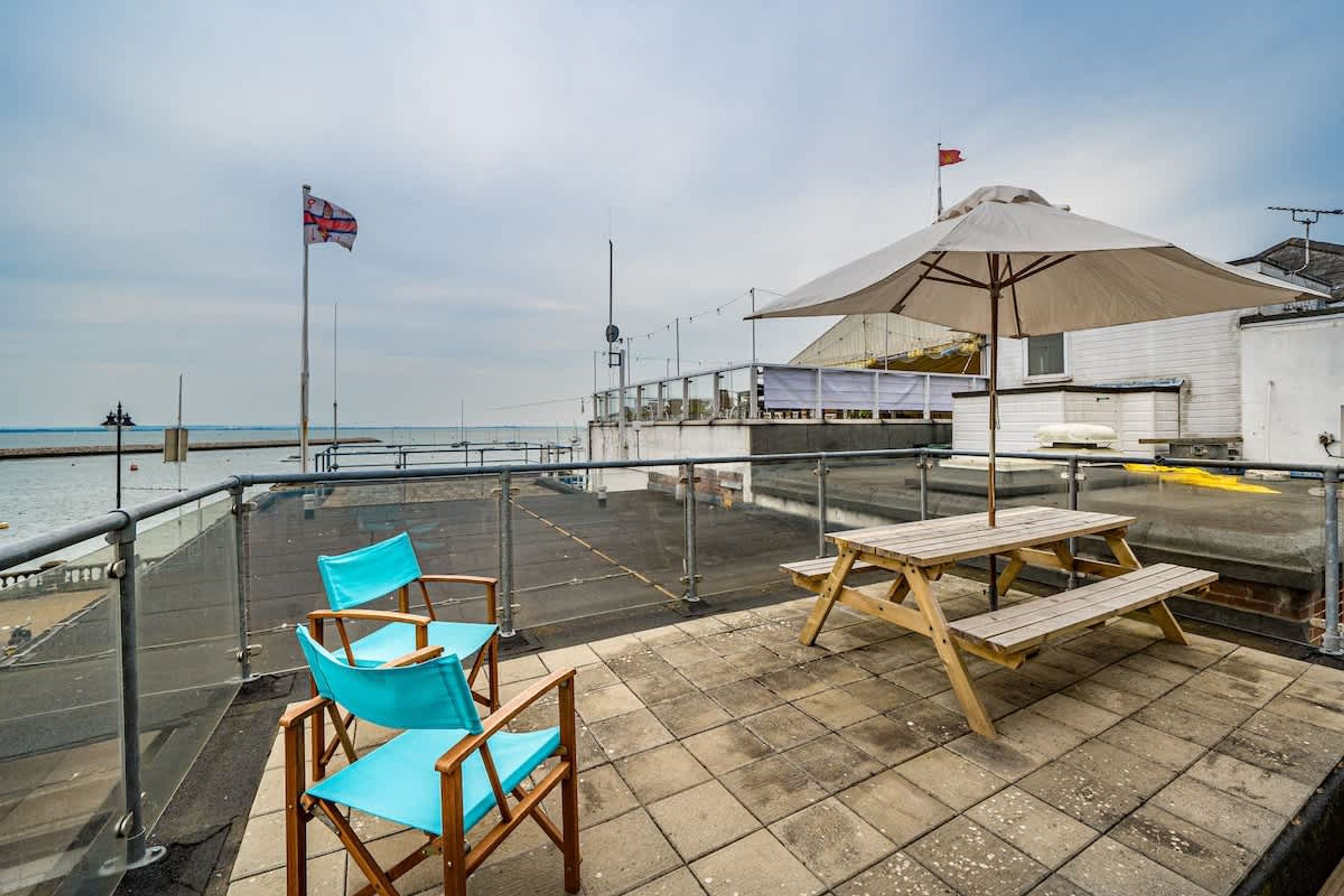A rooftop terrace with a table and chairs, a flag, and a view of the sea.