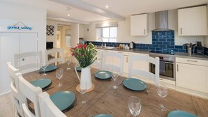 Een moderne keuken met witte kasten, een blauwe betegelde spatwand en een eethoek met teal stoelen en borden.