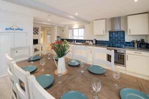 A modern kitchen with white cabinetry, a blue tiled backsplash, and a dining area with teal chairs and plates. - The Watch House Waterfront Home With Solent Views (Cowes)