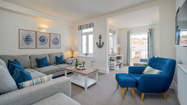 Una sala de estar con un sofá gris, un sillón azul, una mesa de centro y cuadros en la pared.