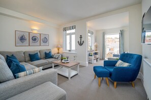Un salon avec un canapé gris, un fauteuil bleu, une table basse et des œuvres d’art encadrées accrochées au mur.