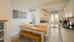 Una cocina moderna con una mesa y banco de madera, armarios blancos y vistas al exterior.