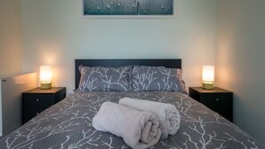 Ein ordentlich bezogenes Bett mit einem gemusterten Bettüberwurf, zwei Nachttischlampen und einem Bild über dem Bett.