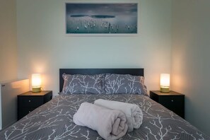 Ein ordentlich bezogenes Bett mit einem gemusterten Bettüberwurf, zwei Nachttischlampen und einem Bild über dem Bett.