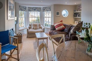 A cozy living room with a sofa, a brown leather couch, a round wooden table, and a blue folding chair. - The Retreat Stylish 4 bed sea Views Parking (Cowes)