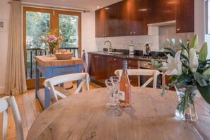 A modern kitchen with wooden cabinets, a dining table with chairs, and a view through the window. - The Retreat Stylish 4 bed sea Views Parking (Cowes)