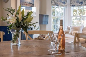 A wooden table with a vase of white flowers, a bottle, and three glasses. - The Retreat Stylish 4 bed sea Views Parking (Cowes)
