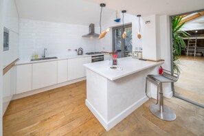 A modern kitchen with white cabinetry, a central island, a stainless steel bar stool, and pendant lighting. - Windchasers Unique 3 bed Duplex With hot tub (Cowes)