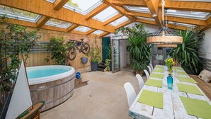 Eine sonnendurchflutete Terrasse mit Whirlpool, Holzdeck und Esstisch mit Stühlen.