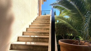 Un escalier en béton menant à un bâtiment à la façade en briques, avec un pot de fleurs et un ciel bleu dégagé.