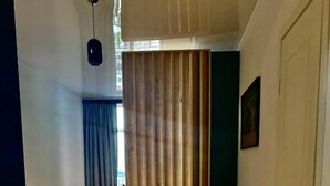 A room with a wooden floor, a red sofa, a bed with a blue curtain, a white door, and a small table with a glass.