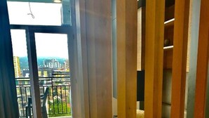 A room with a bed, a wooden partition, and a balcony with a view of buildings and greenery.